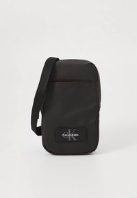 Schwarze Umhängetasche aus Stoff mit rechteckiger Form, ausgestattet mit einem vorderen Logo-Patch, verstellbarem Riemen und glatter Textur.