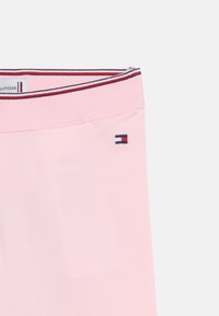 Ροζ ανοιχτή ζώνη μέσης με ριγέ περιθώριο σε κόκκινο, λευκό και μαύρο και μικρό ορθογώνιο λογότυπο σε κόκκινο, λευκό και ναυτικό μπλε στο πλάι.