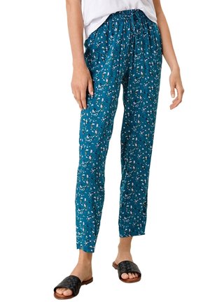 Pantalons à motif floral teal avec une taille élastique, coupe slim et un tissu texturé, associés à des sandales à glisser noires en tissé.