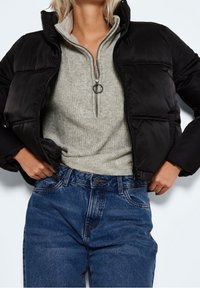 Svart pufferjacka med dragkedja fram, grå höghalssk sweater med kvartdragkedja och blå denimjeans. Anmärkningsvärda texturer inkluderar släta och ribbade tyger.