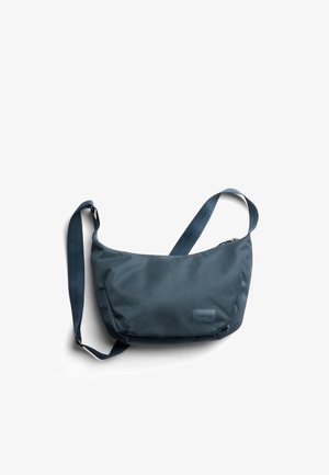 Sac bandoulière en nylon bleu foncé à forme incurvée, avec une sangle réglable et une fermeture éclair. Présente un logo discret en accent.