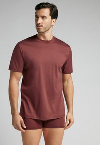 Burgundowa koszulka z krótkim rękawem i okrągłym dekoltem, w połączeniu z dopasowanymi szortami. Gładka tekstura i prosty design.