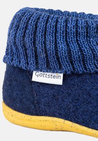 Niebieski, dzianinowy mankiet, ciemnoniebieska, filcowa część główna, żółta, cętkowana podeszwa. Oznaczenie z napisem "Gottstein" pod mankietem. Miękka tekstura w całej powierzchni.
