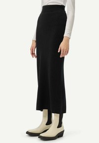 Longue jupe maxi en maille côtelée noire avec une taille haute et des rayures verticales, associée à des bottes à la cheville crème et noires avec un talon épais.