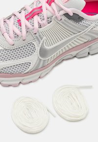 Biało-szary but sportowy z siateczkową cholewką, różowymi akcentami oraz widoczną amortyzowaną podeszwą. Obok leżą dwie białe sznurówki.