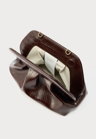 Καφέ σκούρο δερμάτινο τσαντάκι χειρός με μεταλλικά χρυσά εξαρτήματα, μπεζ υφασμάτινη εσωτερική επένδυση και ανοιχτό πάνω μέρος που αποκαλύπτει μια λευκή ετικέτα στο εσωτερικό.