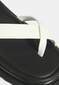 Zwarte flip-flop met een brede witte strap. De voetbed heeft een gladde textuur en de zool heeft een geëxtraheerde grip voor tractie.