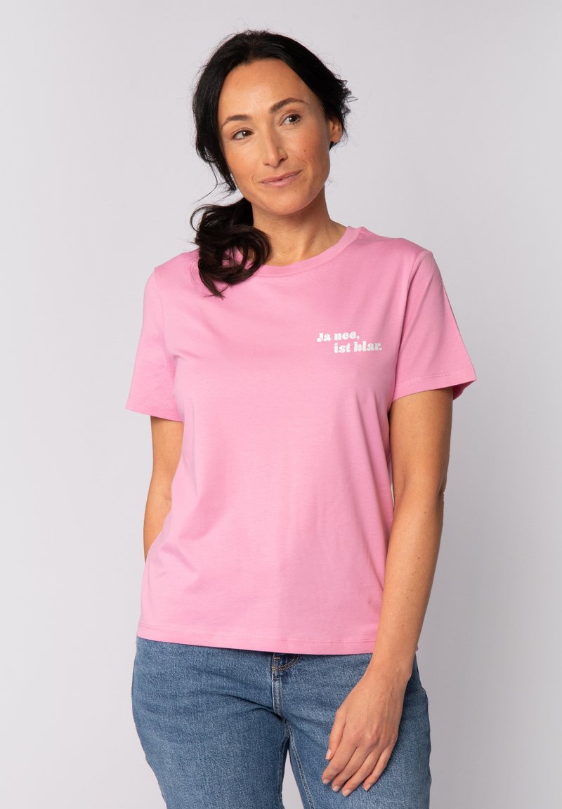 Lichtroze katoenen t-shirt met korte mouwen en een ronde hals; heeft de tekst "Ja nee. is klar." in het wit op de voorkant gedrukt.