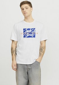 Witte katoenen t-shirt met een blauw en oranje grafisch logo met de tekst "Jack & Jones Essentials" op de voorkant. Casual fit, ronde hals.