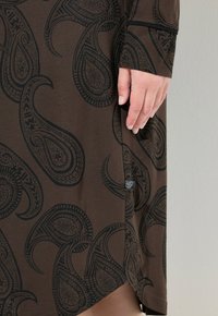 Vestido marrón con estampado de paisley negro, textura suave, mangas largas y una costura lateral con un sutil acento de hardware cerca del dobladillo.