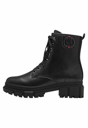 Bottines noires à lacets en cuir avec une semelle en caoutchouc épaisse, arborant un patch logo circulaire et des œillets en métal.
