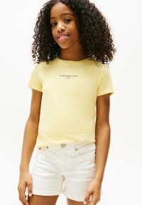 Żółta bawełniana koszulka z krótkim rękawem i okrągłym dekoltem, z logo "TOMMY HILFIGER" w kolorze czarnym. W połączeniu z białymi szortami dżinsowymi.