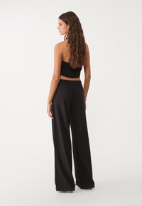 Schwarzes Crop-Top mit strukturierter Oberfläche, kombiniert mit hochtaillierten, schwarzen weiten Hosen, von hinten betrachtet.