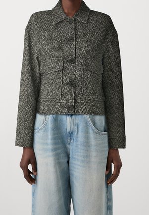 Chaqueta de lana en espiga de color gris oscuro con botones negros y grandes bolsillos delanteros, llevada con jeans de talle alto en azul claro.