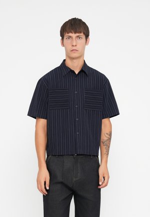 Short-sleeved navy shirt with vertical white stripes, two chest pockets, button front, and a classic collar. Fabric has a smooth texture.