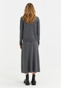 Ensemble en pull gris et jupe longue, texture tricotée, coupe décontractée, poignets et ourlet côtelés, associé à des bottines noires. Vue de dos présentée.