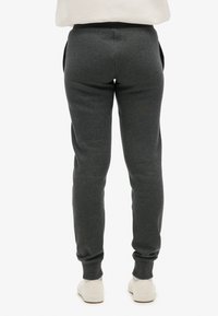 Szare dresy wykonane z miękkiego materiału, z tapered designem, bocznymi kieszeniami i ściągaczem w talii. Gładka tekstura z minimalnymi detalami.