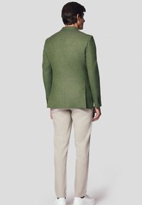 Zielony blazer o fakturze, dopasowany w kroju, w połączeniu z beżowymi spodniami i białymi trampkami. Blazer ma klapki i guziki.