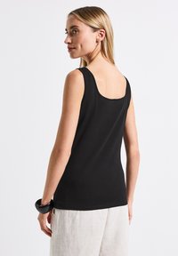 Top senza maniche nero con scollatura rotonda e design aderente. Tessuto di cotone morbido con una texture liscia, abbinato a pantaloni chiari.