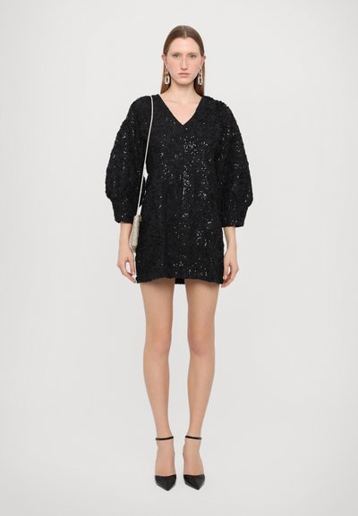 Black sequined mini dress with a V-neck, three-quarter puff sleeves, and a textured finish, paired with black pointed heels.