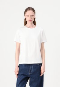 Witte katoenen t-shirt met korte mouwen, ronde hals, losse pasvorm en gladde textuur. G gedragen met blauwe wijde spijkerbroek.