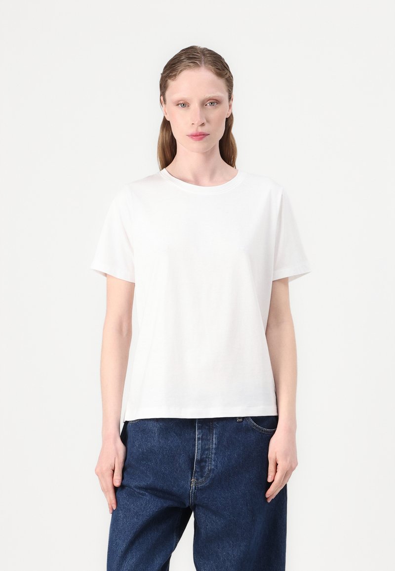 Witte katoenen t-shirt met korte mouwen, ronde hals, losse pasvorm en gladde textuur. G gedragen met blauwe wijde spijkerbroek.