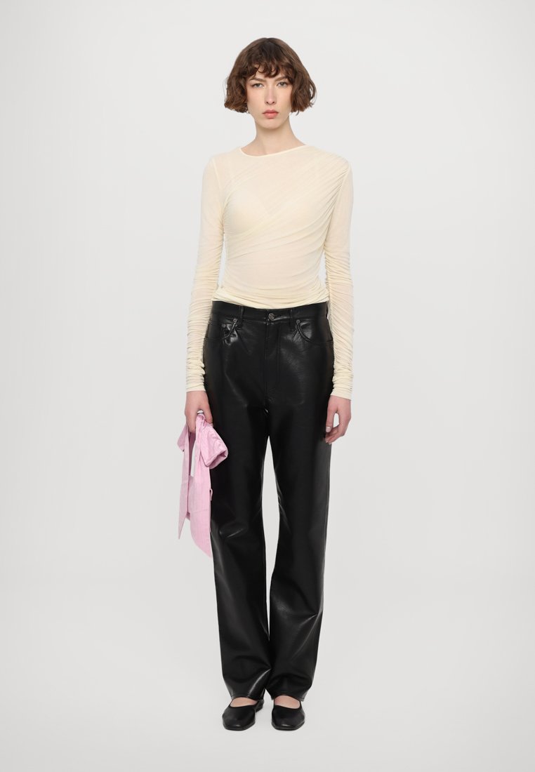 Haut à manches longues transparent en jaune pâle, pantalon large en cuir noir, tenant un tissu rose. Design simple avec peu de matériel, texture lisse.