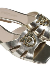 Sandalias deslizantes metálicas plateadas con lados calados y un adorno decorativo de un pájaro dorado y una luna creciente. Textura suave y diseño abierto.