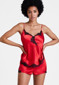 Ensemble de nuit en satin rouge avec de délicates finitions en dentelle noire sur le haut et le short, doté de bretelles ajustables fines et d'une texture douce.