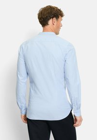 Himmelblaues Langarmhemd mit glatter Textur, abgerundetem Saum, Knopfmanschetten und einem dezenten Streifenmuster, das von hinten sichtbar ist.