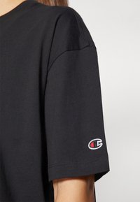 Svart bomull T-skjorte med korte ermer, med brodert logo på ermet. Glatt tekstur og avslappet passform.