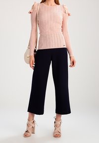 Top a coste rosa chiaro con volant sulle spalle, abbinato a pantaloni larghi blu scuro e sandali chunky con tacco beige.