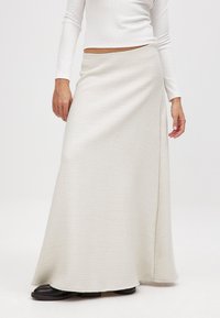 Langer weißer strukturierter Rock im Wickeldesign, aus einem weichen Stoff mit einer fließenden Silhouette, kombiniert mit dunklen flachen Schuhen.