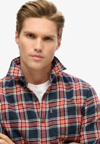 Camisa de cuadros azul y rojo con cuello abotonado, cuenta con un bolsillo frontal y acentos amarillos. Tela suave con un acabado ligeramente texturizado.