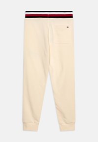 Kremowe dresy z prążkowanym czarnym i czerwonym paskiem w talii, z tylną kieszenią naszytą i zwężającym się krojem nogawki.