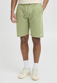 Lysegrønne bomulds-sweatshorts med elastisk talje, snørre, sidelommer og et vævet mærke ved bundkanten.