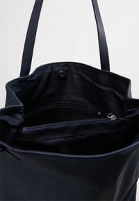 Marinblå tygväska med en mjuk yta, utrustad med två justerbara handtag, innanförs med ett dragkedjefack och ett tryckknappsförslutning för säker förvaring.