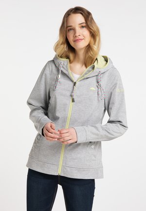 Giovane donna che indossa una felpa con cappuccio grigio chiaro con zip, fodera gialla e coulisse colorate, in piedi con le mani giunte davanti.