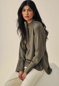 Oliven grøn, bluse med lange ærmer, scoop-neck og knaplukning. Stoffet ser glat ud med let glans og en afslappet pasform.