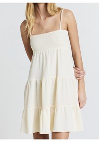 Robe d'été à smocks de couleur crème clair. Sans manches avec fines bretelles, ourlet à volants à étages, tissu texturé et silhouette décontractée pour le confort.