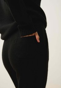 Svart stickad tröja och byxor set, med en mjuk textur, ribbad manschetter och en sidficka på byxorna. Outfiten är åtsittande.