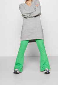 Maglione oversize a costine grigio chiaro con scollo a V, abbinato a pantaloni svasati a costine verde brillante e scarpe da ginnastica nere e argento.