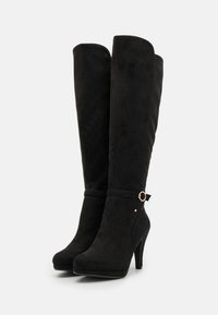 Black knee-high boots made of soft suede, featuring a high heel, a rounded toe, and a gold accent near the ankle with a strap detail.