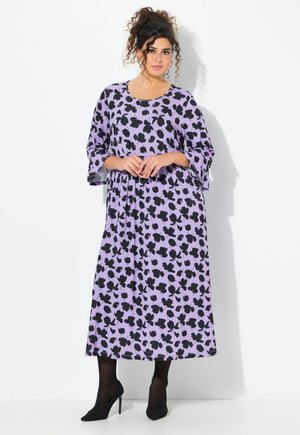 Langes, lila Kleid mit schwarzen Blumenmustern, weiten Ärmeln und einem runden Ausschnitt. Kombiniert mit schwarzen High Heels und Strumpfhosen.