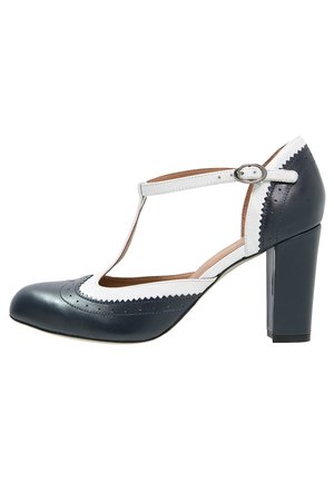 Black and white T-strap high heel shoe with buckle closure, rounded toe, and scalloped trim detailing.