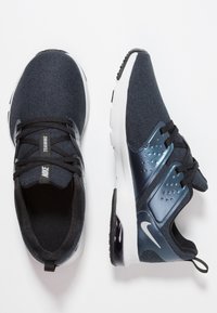 Dark blue Nike training sneakers with black laces, white soles, and a visible air cushion on the heel, shown from top and side views.