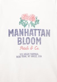 Bílý tričko z látky s růžovými a zelenými grafikami růží nad nápisem "MANHATTAN BLOOM" v tučném modrém písmu. Obsahuje adresu firmy níže.