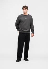 Γκρι φούτερ με στρογγυλή λαιμόκοψη και ριμπ μανσέτες. Συνδυασμένο με φαρδιά μαύρα παντελόνια και μαύρα παπούτσια. Διαθέτει μικρό λογότυπο στο στήθος.