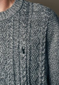 Suéter gris de punto con un patrón texturizado que incluye trenzas y diseños en zigzag. Cuello redondo con remate acanalado.