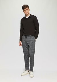 Zwarte lange mouw polo gecombineerd met grijs geruite broek en witte sneakers. Lichtgewicht stof, aansluitende pasvorm en een trekkoord in de taille.
